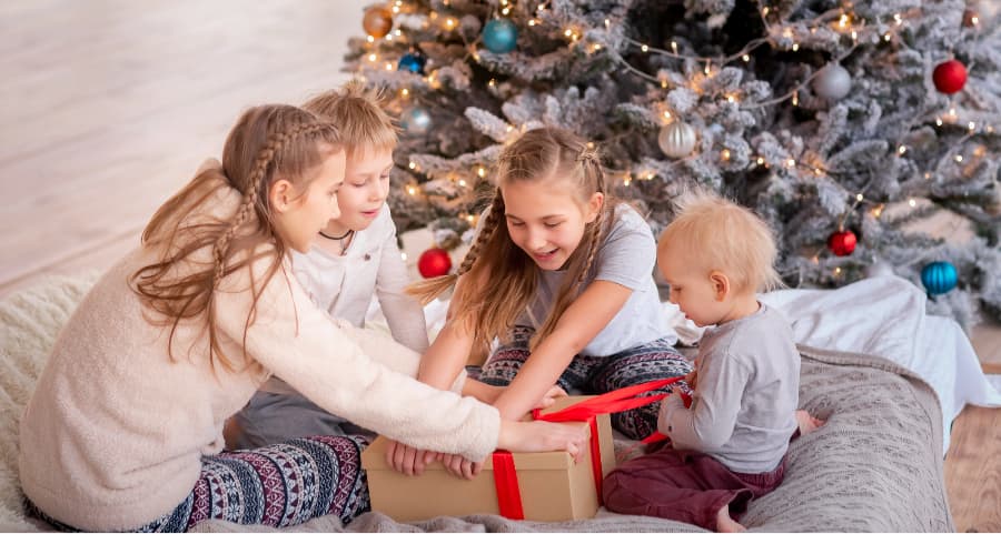 Siblings opening a gift near a Christmas tree.